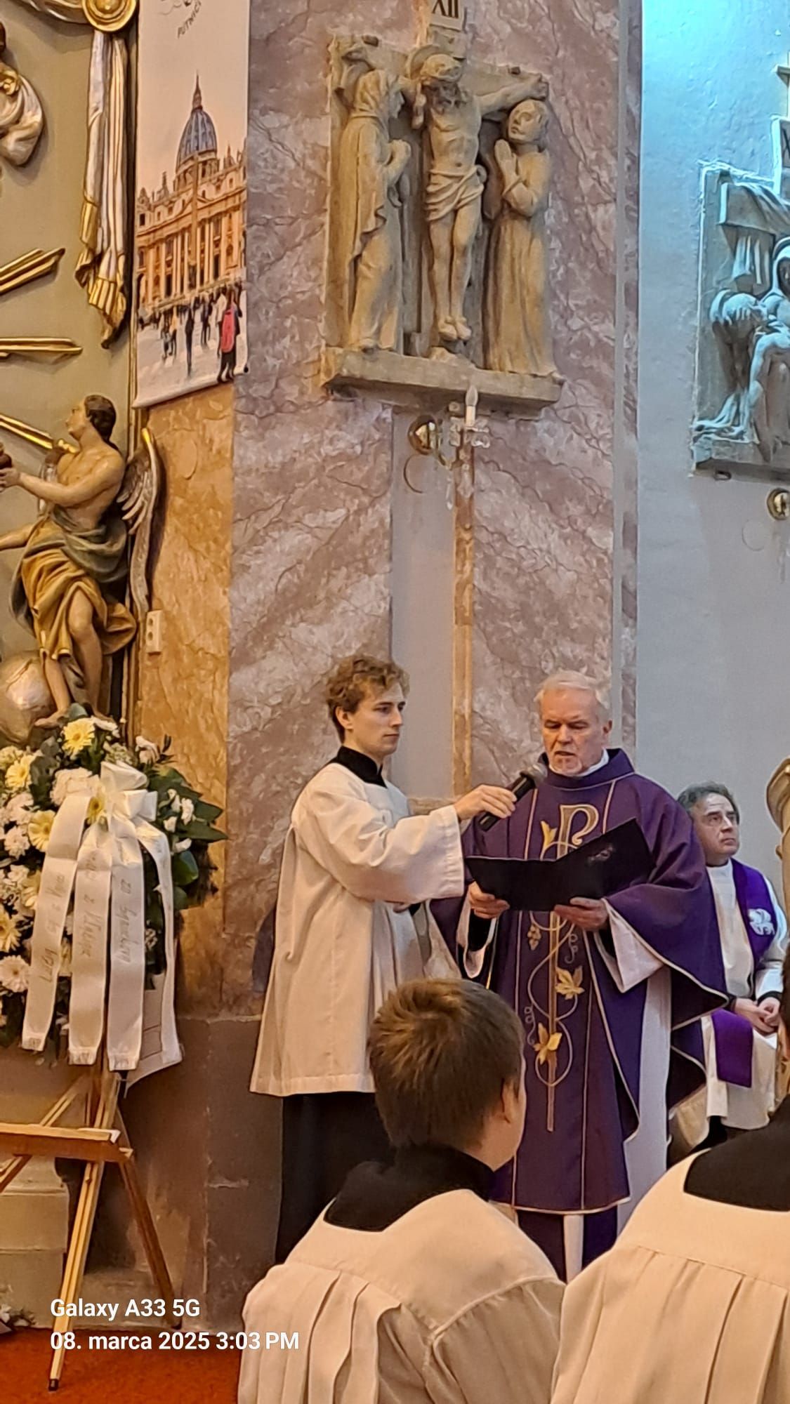 Pohľad do interiéru kostola počas pohrebnej omše Mons. Mariána Feduša v Rišňovciach, 8. marca 2025. Okolo oltára kňazi v liturgických rúchach fialovej farby a miništranti, na pozadí oltár s bohatou výzdobou a svietiacim lustrom nad ním.