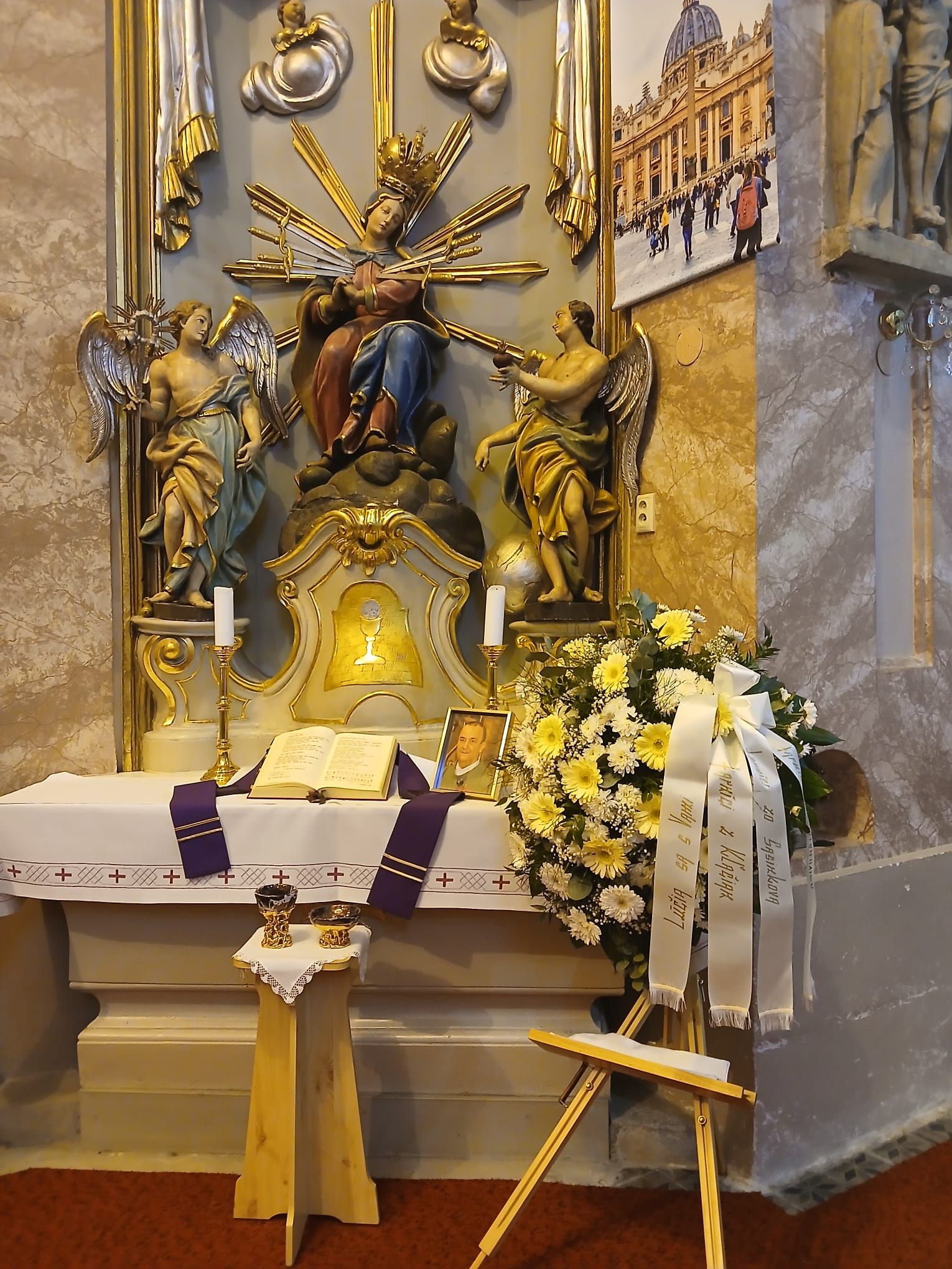 Pohľad do interiéru kostola počas pohrebnej omše Mons. Mariána Feduša v Rišňovciach, 8. marca 2025. Okolo oltára kňazi v liturgických rúchach fialovej farby a miništranti, na pozadí oltár s bohatou výzdobou a svietiacim lustrom nad ním.