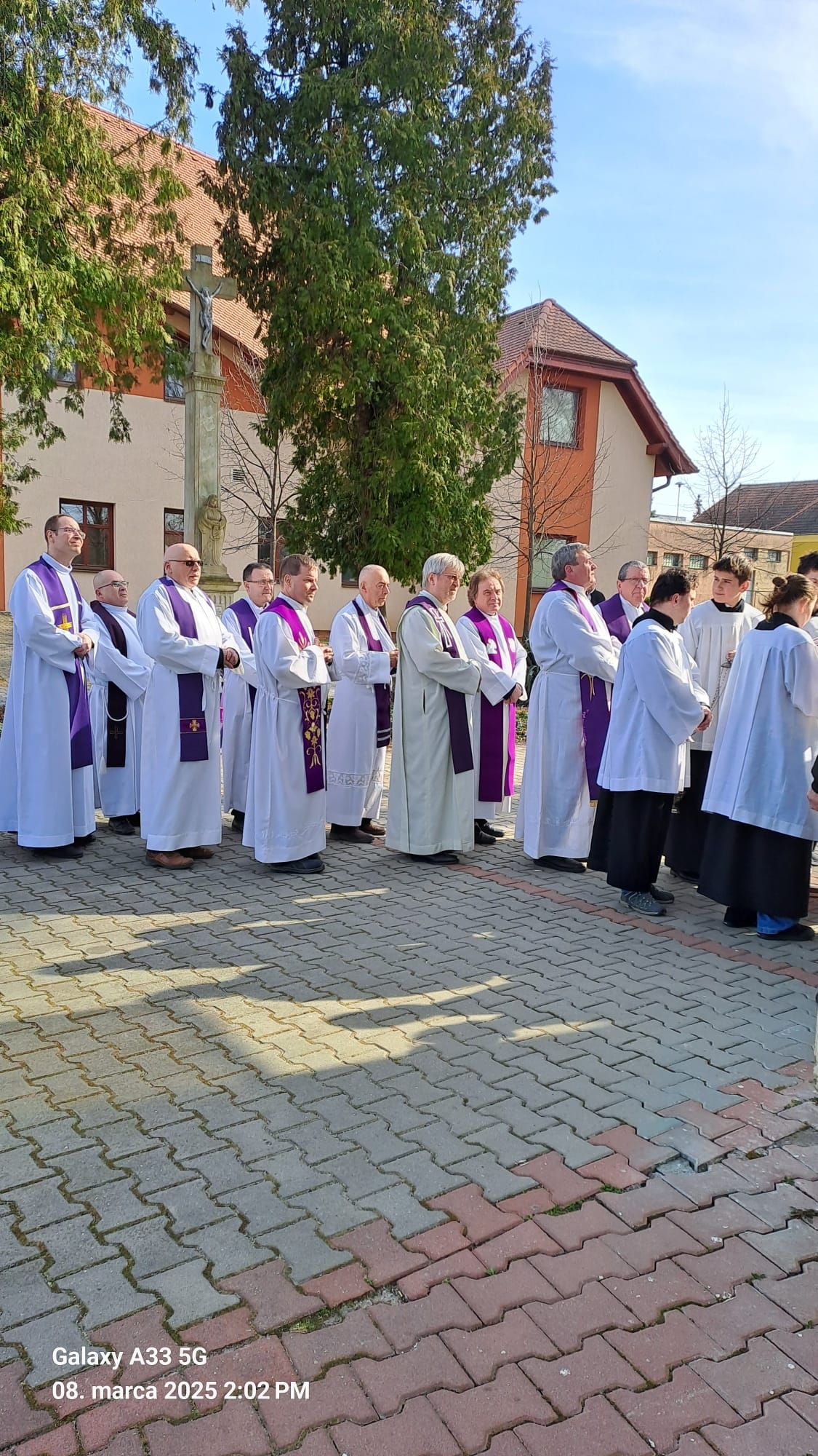 Pohľad do interiéru kostola počas pohrebnej omše Mons. Mariána Feduša v Rišňovciach, 8. marca 2025. Okolo oltára kňazi v liturgických rúchach fialovej farby a miništranti, na pozadí oltár s bohatou výzdobou a svietiacim lustrom nad ním.