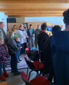 Ľudia v pastoračnom centre s farárom a miništrantmi pri požehnávaní. 