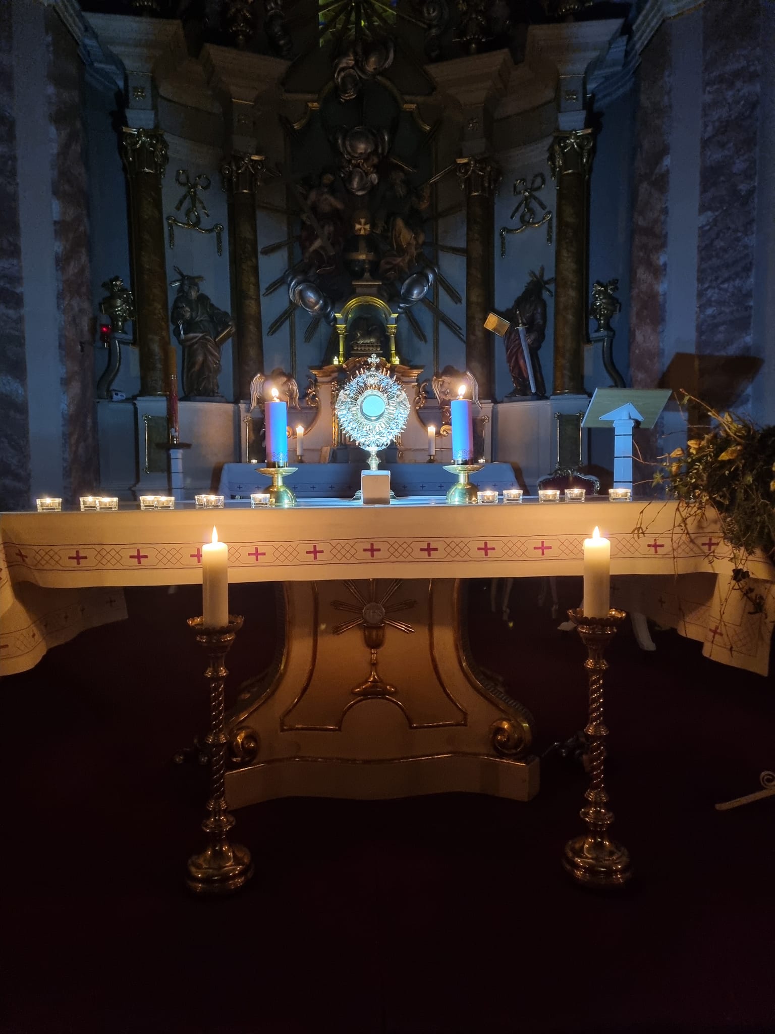 Adventná adorácia vo Farskom kostole Najsvätejšej Trojice v Rišňovciach, s vyloženou Eucharistiou na osvetlenom oltári, adventným vencom a zapálenými sviečkami v prítmí kostola